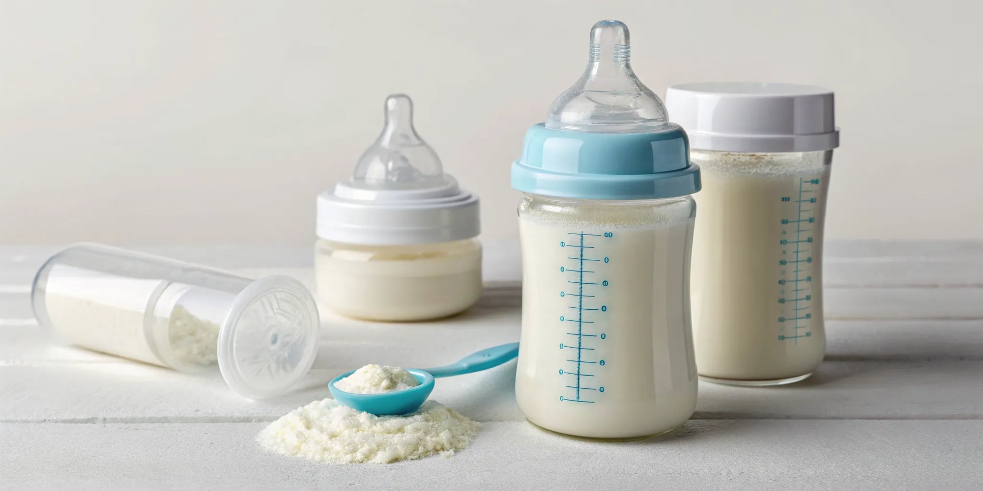 A scoop of baby formula powder and bottles for different feeding stages.