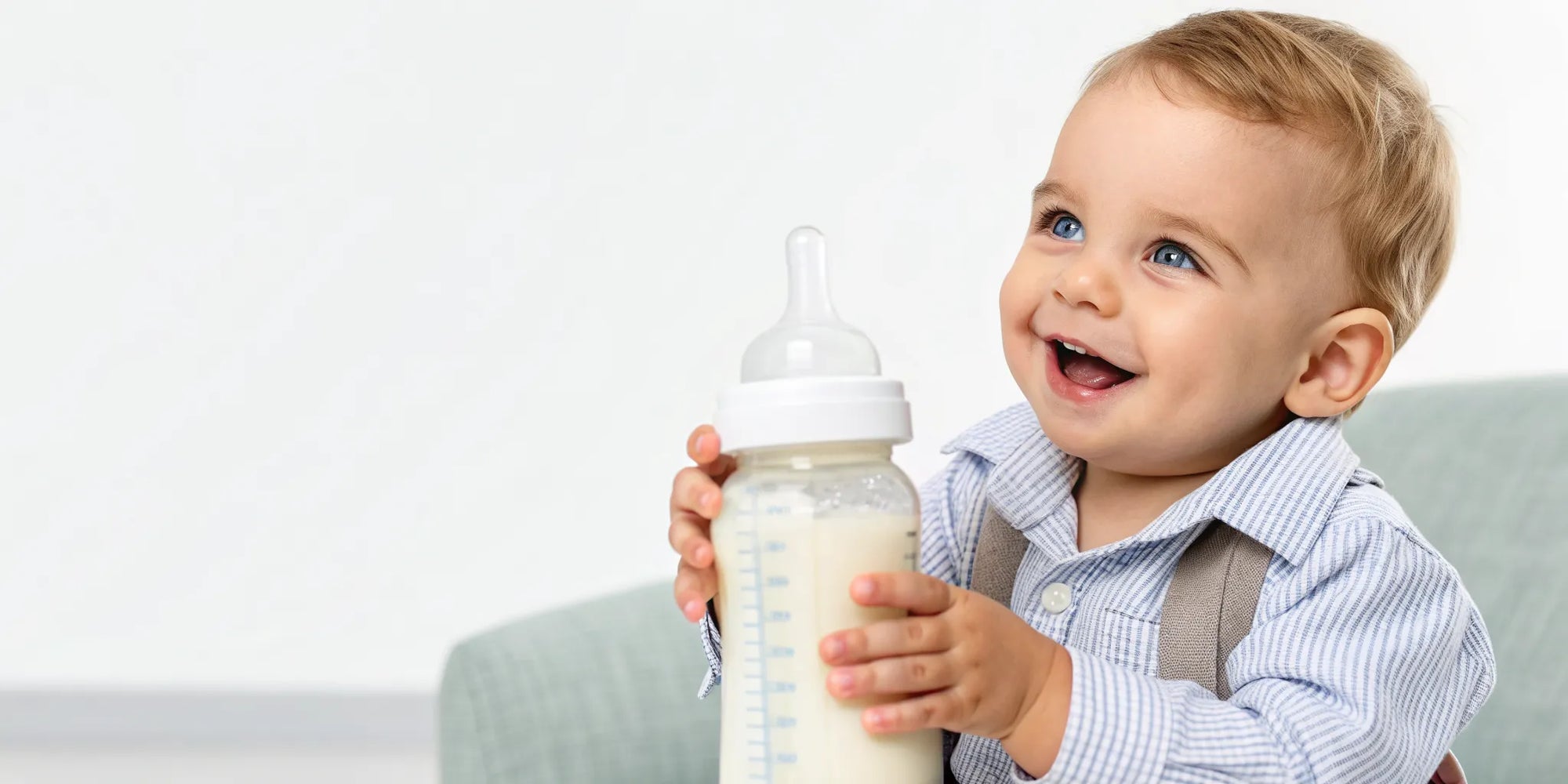 Smiling toddler holding a bottle of toddler formula for a sensitive stomach.