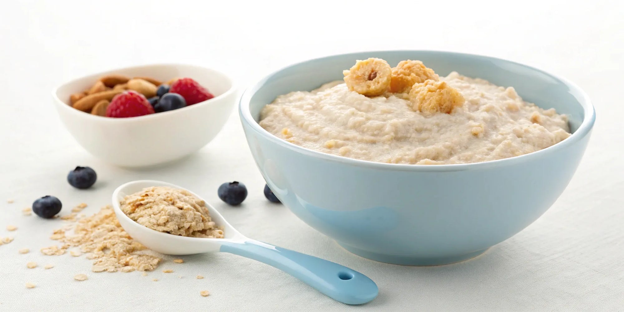 A baby's first bowl of infant cereal with a spoon and fresh berries.