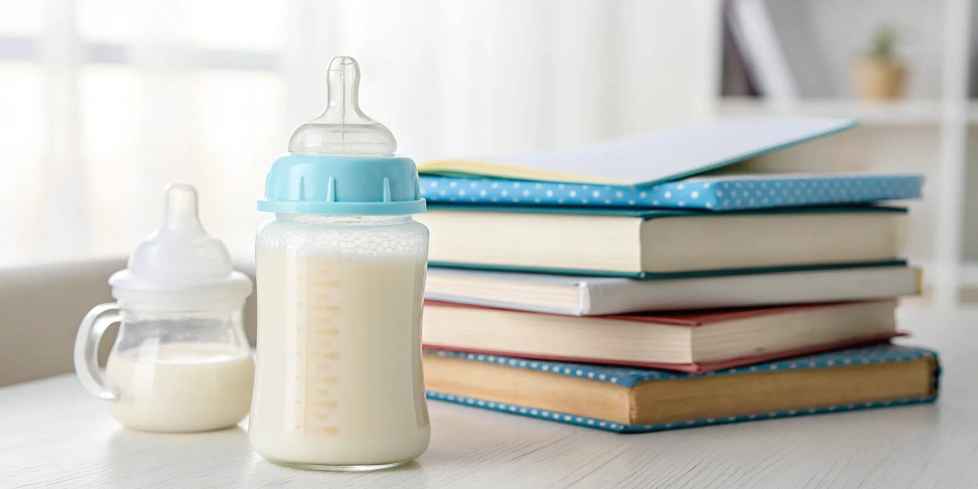 Several baby bottles containing hydrolyzed formula next to a stack of books.